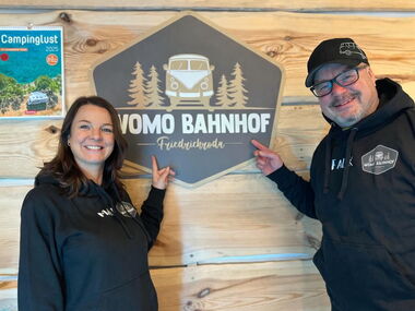 Herr und Frau Falk Betreiber Wohnmobilstellplatz Friedrichroda vor Logo
