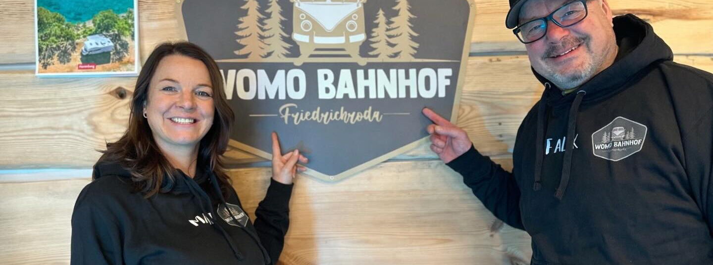 Herr und Frau Falk Betreiber Wohnmobilstellplatz Friedrichroda vor Logo